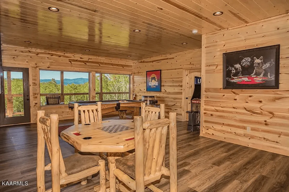 A bright, inviting game room combines a wooden dining table and a classic pool table, both set beside large windows offering mountain views. The space is tailored for family gatherings, lively game nights, and friendly competition, all in a relaxed setting.