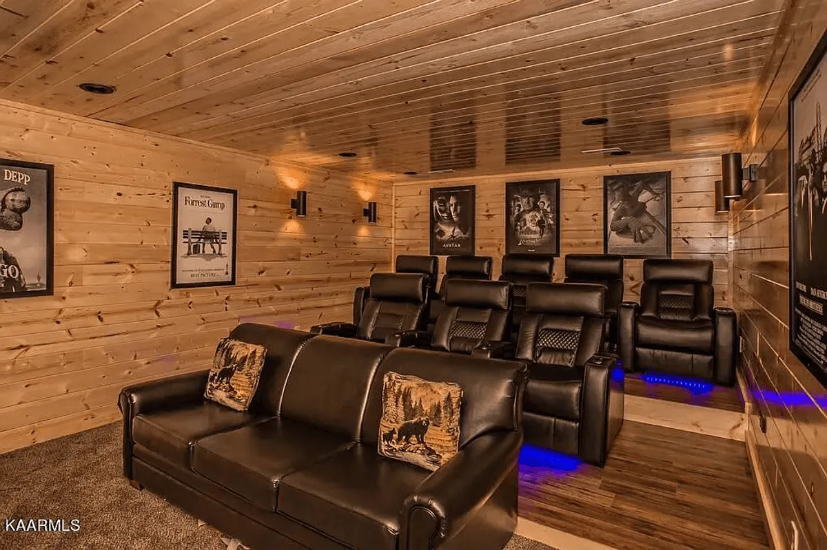 A stylish home theater room with plush leather recliners, warm wood paneling, and eye-catching movie posters on the walls. The cozy couch with decorative pillows invites guests to settle in for family movie nights or epic film marathons.