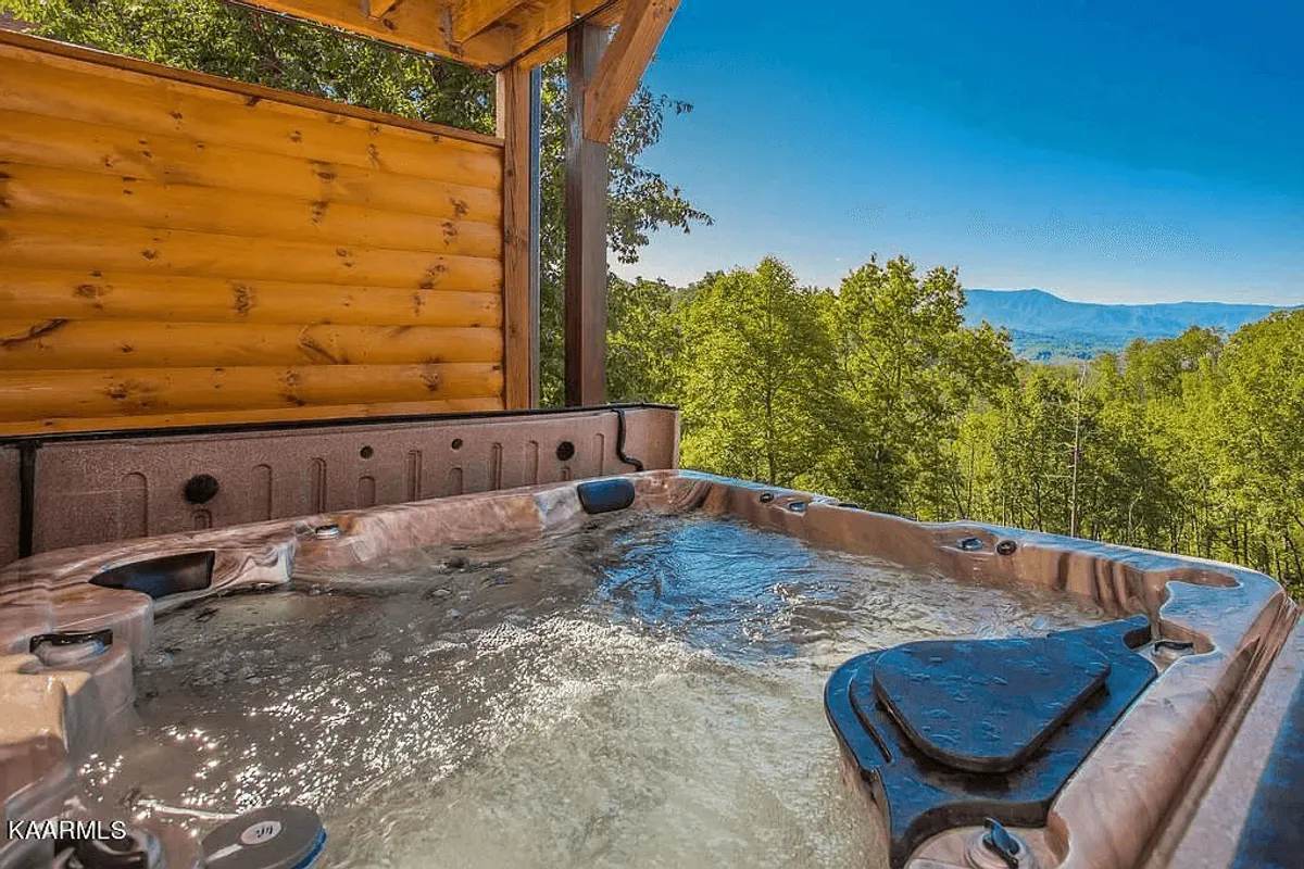 An outdoor hot tub nestled among trees, with mountain views visible in the background. The tranquil setting invites guests to soak, relax, and savor the fresh mountain air—especially under the stars.