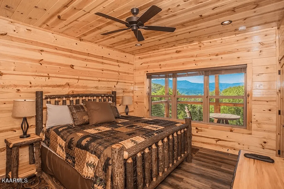 A bedroom with a wooden bed frame dressed in plaid bedding, large window offering a stunning mountain view, and nightstands with soft lighting. The room feels tranquil and connected to nature.