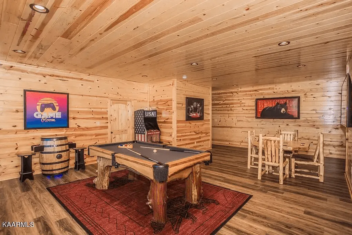 An open-concept interior featuring a pool table, wooden dining set, and a barrel table, surrounded by artwork. The setting emphasizes social interaction and communal activities, located adjacent to kitchen and living areas.