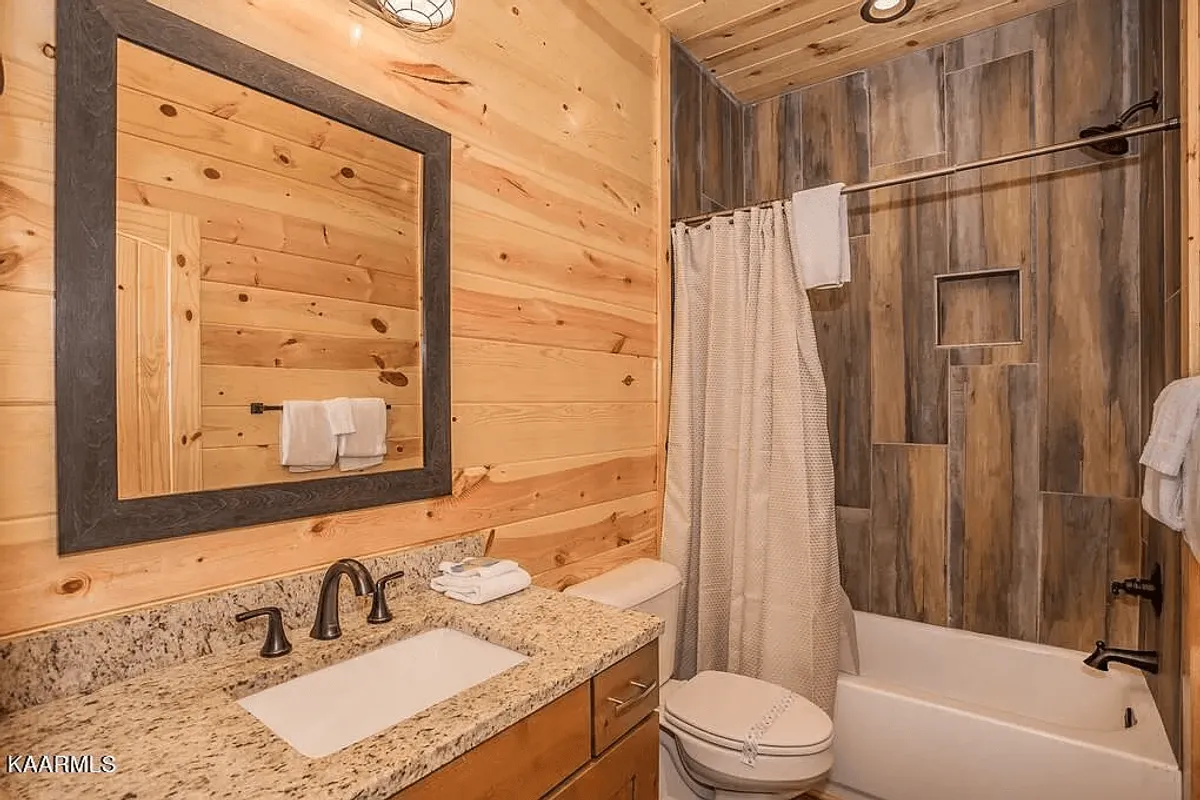 A warm, inviting bathroom with wooden wall panels, a granite countertop, and a stylish mirror. A shower curtain hints at a soothing bath or refreshing shower, with plush towels completing the spa-like vibe.