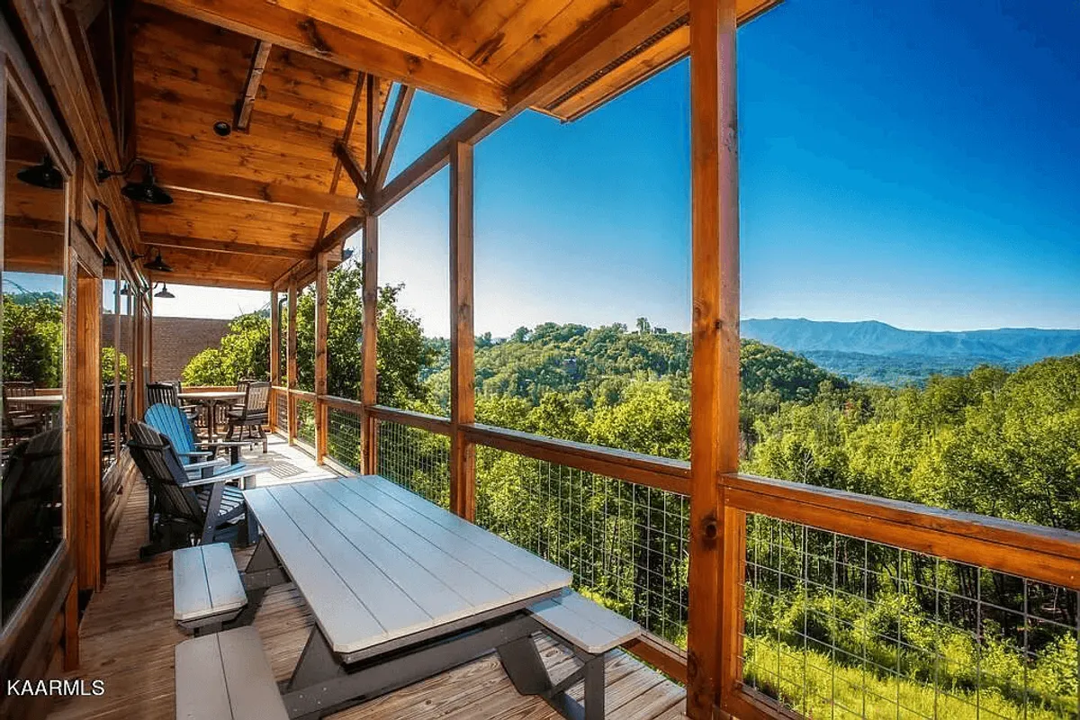 A wooden deck with comfortable outdoor seating and a table overlooks sweeping mountain views. The scene suggests moments spent dining, socializing, or simply soaking in the breathtaking surroundings, seamlessly blending the indoor luxury experience with the natural world beyond.