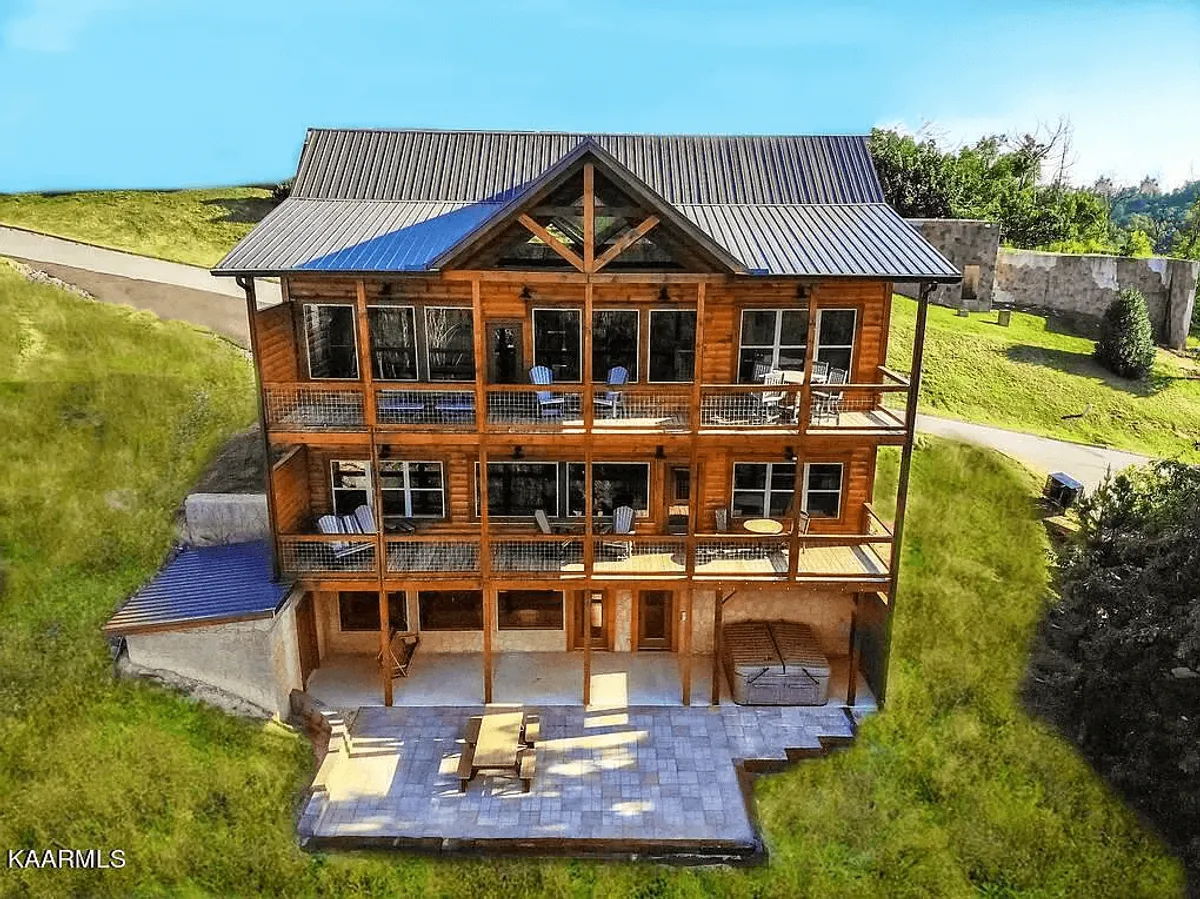 The image showcases the exterior of a stunning wooden cabin set against a backdrop of the Smoky Mountains. Large windows and spacious balconies offer panoramic sunset views, with inviting outdoor seating perfect for family gatherings, dining, and relaxing amidst nature.