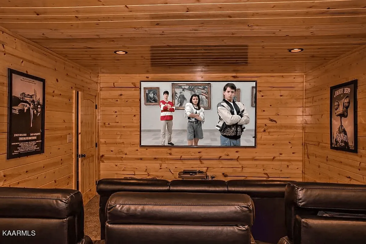 A cozy, dedicated home theater room with a large screen television playing a classic film, plush leather seating, and vintage movie posters. The wood-paneled walls add rustic charm and a sense of gathering for memorable family movie nights.